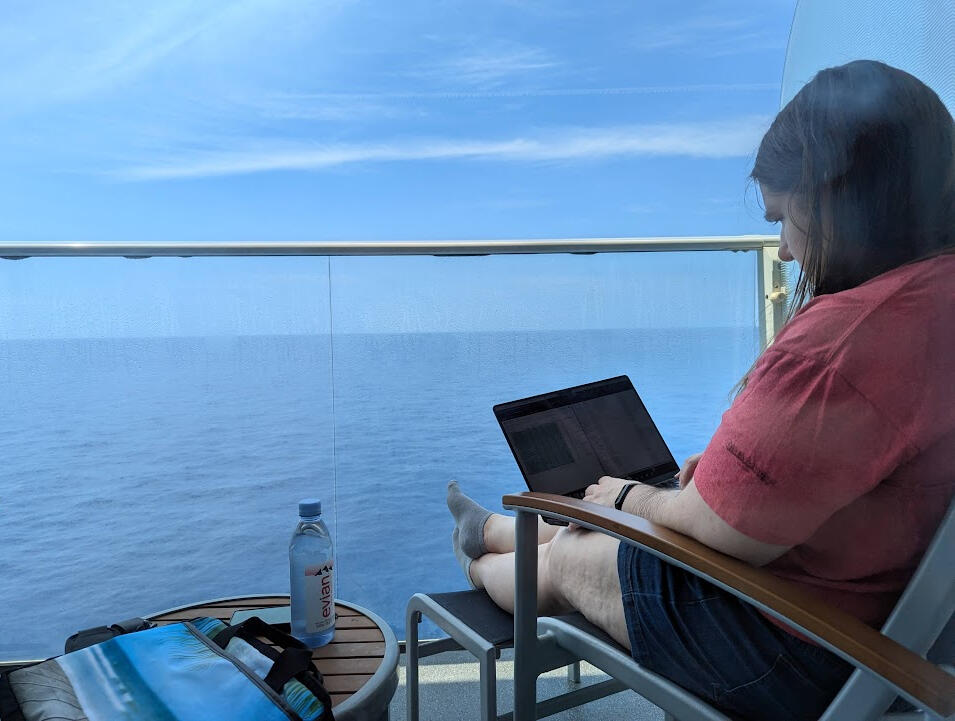 A writer's laptop screen with a sun setting on open ocean behind it.