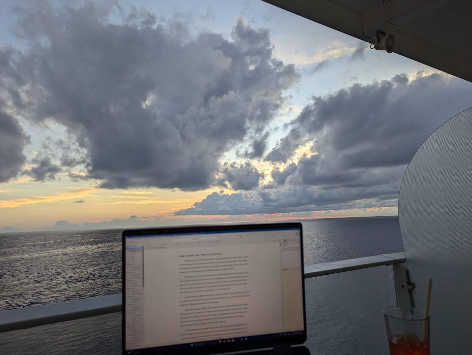 A writer's laptop screen with a sun setting on open ocean behind it.